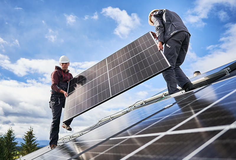 2 Mitarbeiter tragen Solarmodule für eine PV-Anlage über ein Dach